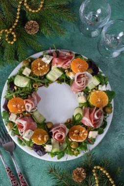 Yeşil tatil arka planında çelenk şeklinde salata, mandalina, roka, mavi peynir, salatalık ve çam fıstığı.