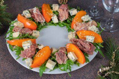 Beyaz tabakta Hamon, hurma, roka ve doru peynirli salata.