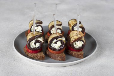 Domatesli kanepeler ve sarımsaklı patlıcan ruloları ve gri tabakta krem peynir.