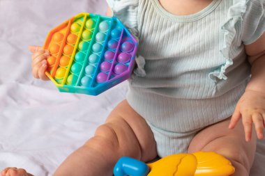 Sekiz aylık bir çocuk yatakta otururken renkli oyuncaklarla oynuyor.