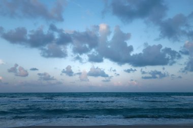Derin mavi gökyüzü ve esinti dalgalarıyla sakin okyanus kumsalı alacakaranlığı.
