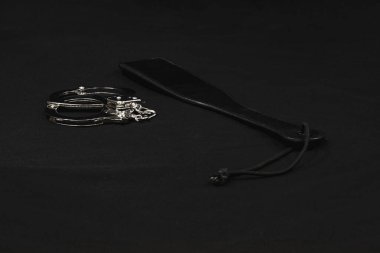 Bir çift kelepçe ve siyah bir arka planda şaplak. BDSM