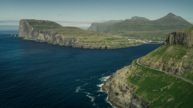 Gündüz vakti Faroe Adaları 'ndaki Risin og Kellingin kaya oluşumlarıyla Eysturoy adasının sahil şeridinde panoramik manzara. Güneş ve mavi gökyüzü, mavi okyanus ve yeşil uçurumlar.