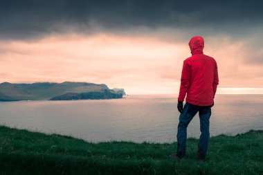 Faroe Adaları, gün batımında Eysturoy 'daki kayalıklara bakan kırmızı ceketli adam.