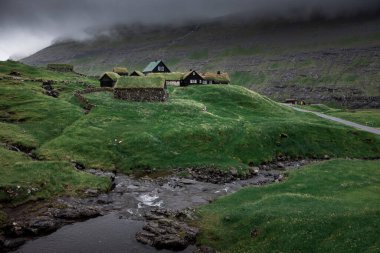 Streymoy Adası 'ndaki Saksun köyünde çim çatılı ve şelaleli kulübeler, Faroe Adaları' nın önünde nehir.