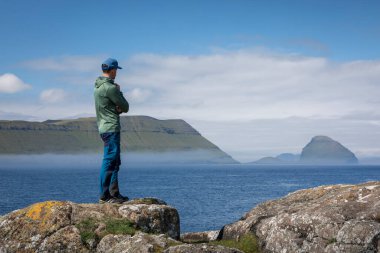 Faroe Adaları 'nın güneşli adalarına bakan bir kayanın kıyısındaki adam.