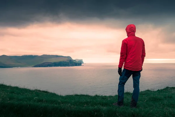 Faroe Adaları, gün batımında Eysturoy 'daki kayalıklara bakan kırmızı ceketli adam.