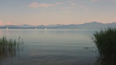 Bavyera 'daki Chiemsee Gölü' nde yaz boyunca tekneler ve Alp dağları, sakin su ve gün batımı