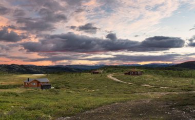 Huts in landscape of Norway during sunset clipart
