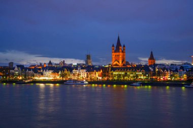 Gece Köln 'de ortaçağ seti ve Cat. Yüce St. Martin Kilisesi. Aydınlatılmış binaları (mimarisi) ve nehir kıyısı boyunca tekneleri olan Idyllic şehir manzarası.