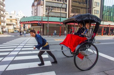 03-22-2015 Tokyo. Tokyo 'da bir çocuk (rickshaw) kavşakta kırmızı ışıkta yol üstü yolculara geziye başlıyor. Oğlan ve gülümseyen yolcular.