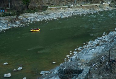 Rafting: Tekne Beas Nehri 'nin sakin bir yakasında ilerliyor. Himachal Pradesh 'teki Kullu kasabasının yanında. Hizmetli tekneyi kendisi kontrol ediyor, diğer turistler de ödeme ve selfie yapıyor. Tanınmayan kişiler.