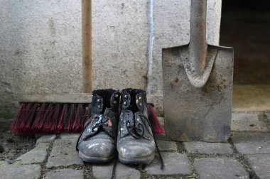 old worn painted work boots with a yard broom and a spade as symbol for cleaning, house keeper or maintenance clipart