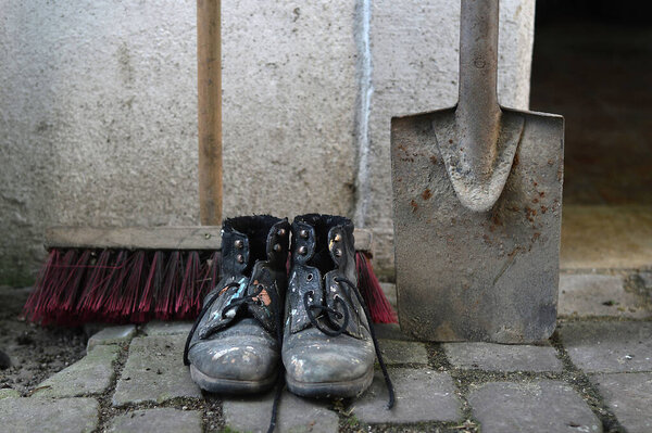 old worn painted work boots with a yard broom and a spade as symbol for cleaning, house keeper or maintenance