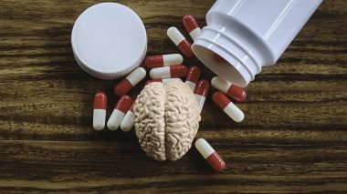 Minyatür Beyin Modeli ve Ahşap bir yüzeydeki şişeden dökülen kırmızı ve beyaz haplar, Zihinsel Sağlık, Nörolojik Bozukluklar ve Psikiyatri Tedavisi.