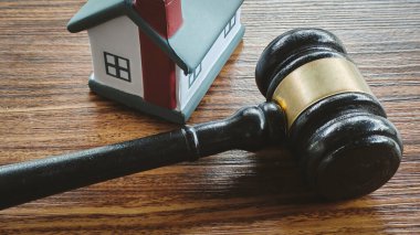 Gavel Tahta Yüzeyde Minyatür Ev Modelinin Yanında Yatıyor, Gayrimenkul Kanunu, Mülk Anlaşmazlıkları, Haciz ve Konut Yasası 'nı Sembolize Ediyor.