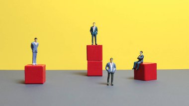 Kırmızı blokların üzerinde duran minyatür iş adamları kariyer büyüme hiyerarşisi ve liderlik yarışmasını gösteriyor