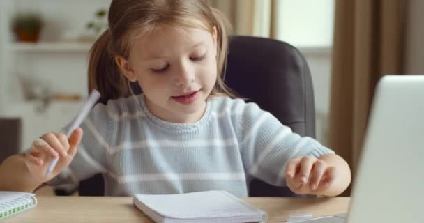 Little school girl pupil teach mathematic or painting drawing in school online. Distance education at home, online e-learning. Cute child looking in laptop screen sitting at table writing in notebook — Stock Video