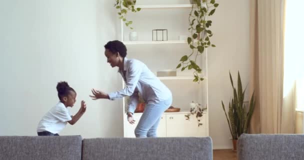 Afrikaanse familie, jonge moeder met leuke grappige dochter spelen in de woonkamer, vrouw raakt kind door handen, vangt knuffels en kringen kid, mam en klein meisje veel plezier thuis samen, gelukkige jeugd — Stockvideo