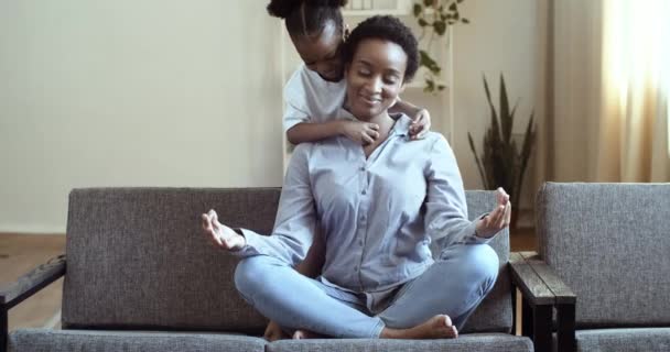 La fille africaine maternelle active chatouille la mère ethnique assise en position lotus pratique la maîtrise de soi se sentir serein calme, réduire la fatigue du stress pendant la journée à la maison avec peu d'enfants métis — Video