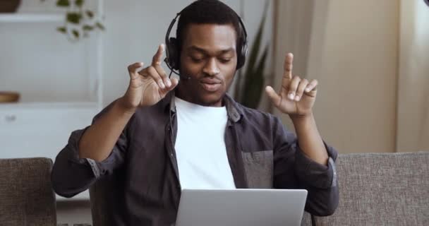 Retrato de relaxado alegre homem de negócios africano usar fones de ouvido sem fio desfrutar ouvir música som sentar no sofá, jovem trabalhador estudante fazer uma pausa em casa se sentir feliz, dança despreocupada com a mão — Vídeo de Stock