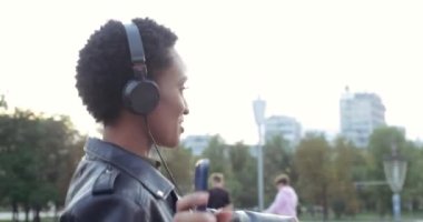 Hafta sonu şehirde kulaklıkla gezen, akıllı telefondan modern müzik dinleyen, sokakta yüksek sesle şarkı söyleyen, tasasız gençlik konsepti olan Afrikalı genç bir kadının yan görüntüsü.
