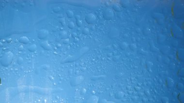 Sıçramalar, bulanık damlalar ve mavi gökyüzünde girdaplar ve parlak güneş arka planı. Su dengesi. Kozmetik tazelik prosedürleri. Temizlik kavramı, vücut bakımı. Nemlendirici temiz sıvı kullanımı..