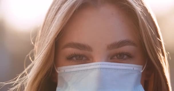 Крупным планом женское лицо в маске смотрит в камеру, молодая девушка в маске защищает свой рот от вирусной инфекции респираторных заболеваний, коронавируса эпидемии времени, леди на открытом воздухе портрет — стоковое видео