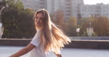 Yalnız, güzel, sarışın bir kadın, gündelik kıyafetlerle ve uzun saçlarıyla şehrin göbeğinde güneş ışığında dönüyor. Güzel bir kız. Moda mankeni. Uçan saç modeli.