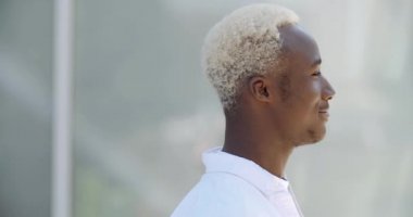 Çekici Afro-Amerikan erkek öğrenci dışarıda poz veriyor beyaz elbiseler giyiyor, elleri kameraya doğru dönüyor ve neşeyle gülümsüyor.