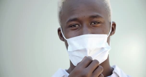 Close-up portret Afrykanin amerykański człowiek student mieszane rasy facet zdejmuje maskę medyczną z męskiej twarzy uśmiechając się czuje triumf i ulga bezpieczeństwo stoi na zewnątrz, koniec pandemii wirusa, zwycięstwo nad covid — Wideo stockowe