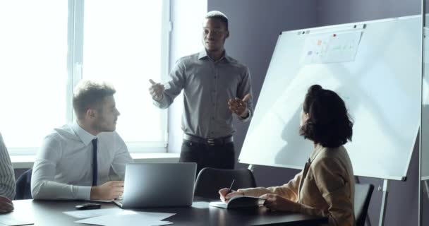 Afrikansk affärsman gruppledare presenterar projektstrategi visar idéer om whiteboard på kontoret för kollegor, tre personer medarbetare sitter vid bordet i konferens njuter av utbildning seminarium — Stockvideo