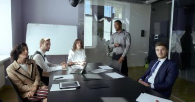 Kurumsal toplantı odasında oturan çok ırklı ortaklar grubu, erkek Afrikalı analist projenin sunumu için dijital etkileşimli beyaz tahta kullanıyor, avukat yatırımcılar ekrana bakan