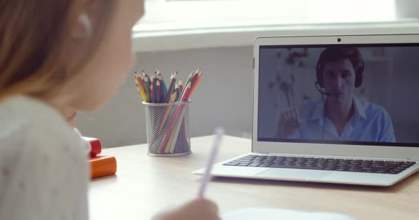 Boční pohled běloška základní školy dívka nosí sluchátka se podívat na notebook vzdálenost učení doma. Zaměřené roztomilé dítě poslech audio lekce on-line video studium u stolu domácí úkol dálkové — Stock video
