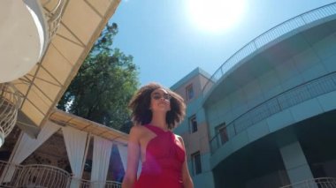 Amerikan modasına uygun bir kadın yavaşça kameranın önünden geçiyor, gökyüzünde güneşli bir siluet, kıvırcık saçlı, otelin havuzunun yanındaki plajda yaşayan Afrikalı etnik kökenli bir kız, yaz tatilinin tadını çıkarıyor.