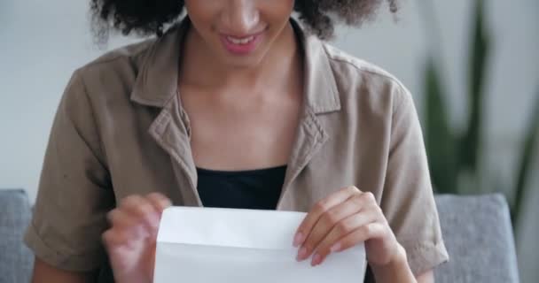 Foto de la cabeza feliz mujer africana lee buenas noticias en carta de correo se sienta en el sofá en casa, celebrando el éxito. Ganadora americana sostiene papel bancario recibiendo préstamo aprobado, reembolso de impuestos o aviso de salario — Vídeos de Stock