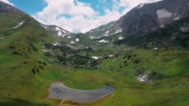 Létání nad krásným svahem Kavkazské zasněžené hory s malým lesem, kameny pod mraky na obloze v letním slunném počasí. Krajina letecký pohled na nádherné horské přírody. — Stock video