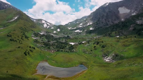 Volando hacia adelante sobre la hermosa ladera de la montaña de nieve caucásica con un pequeño bosque, piedras bajo nubes en el cielo en verano tiempo soleado. Paisaje vista aérea de la maravillosa naturaleza de montaña. — Vídeos de Stock