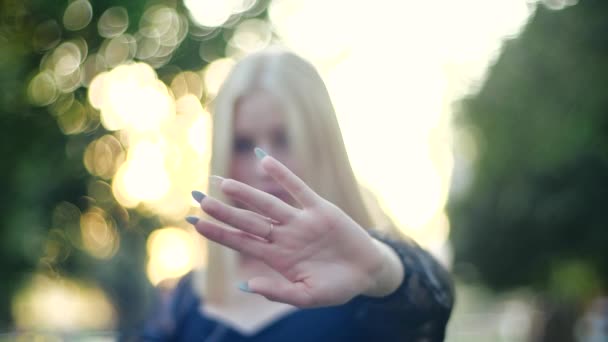 Силуэт девушки в черном платье на фоне деревьев и солнца, отгораживающейся обеими руками аккуратным маникюром и золотым кольцом от блокирующей камеры, показывающей знак "стоп", протестующей. — стоковое видео