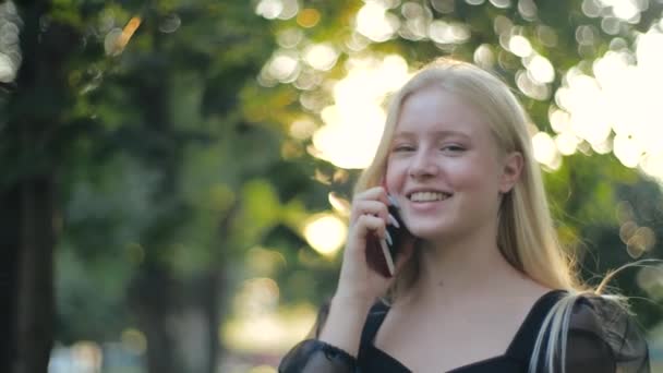 Ragazza adolescente felice con i capelli biondi e manicure parlando al telefono e sorridendo. Comunicazioni mobili e in quarantena, amicizia e romanticismo, amore. Donna allegra passeggiate nel parco, stile di vita sano. — Video Stock