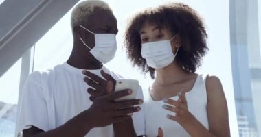 Afrikalı genç adam ve kadın beyaz kıyafetler giyer ve yüzlerine koruyucu tıbbi maskeler takar. İnternet 'te bilgi arayan modern cihazlara bakın. Aktif olarak tartışılmış haberleri okuyun.