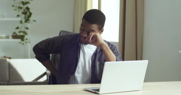 Африканский уставший мужчина фрилансер, сидящий за столом за компьютером в домашнем офисе, глядя на экран ноутбука, испытывая напряжение, сожаление трет глаза, держа мост носа от переутомления, ошибка концепции — стоковое видео