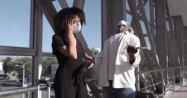 Curly mixed race girl woman wife and african boyfriend man husband wear protective medical masks stand at airport terminal station with luggage, cancellation of flight due to virus pandemic feel rage — Stock Video