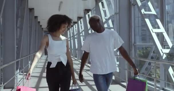 Para afrykańskich nastolatków dziewczyna i facet idąc ulicą miasta z zakupami trzymając torby z prezentami i nowe ubrania kupione z rabatem na czarny piątek, zakupoholicy szczęśliwie taniec świętować sprzedaż — Wideo stockowe