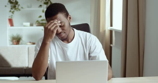 Afrikai férfi szabadúszó diák visel fehér ül az asztalnál nézi laptop úgy érzi, szenved fejfájás migrén tünetek vírus betegség orvosi segítségre van szüksége, olvassa rossz hír megoldja nehéz probléma — Stock videók