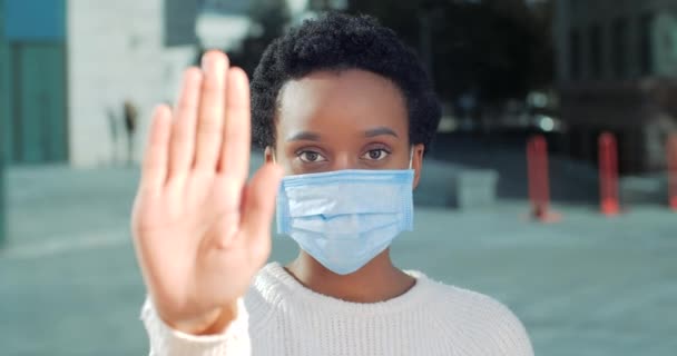 Hand-Stoppschild in der Nähe. Afrikanerin mit steriler medizinischer Maske im Gesicht, zeigt bei Ausbruch des Coronavirus Distanzgeste, legt Handfläche vor sich, um Ausbreitung der Epidemie zu verhindern — Stockvideo