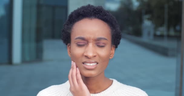 Close-up portret van Afrikaanse gemengde ras etnische vrouw buiten staan gevoel kiespijn slechte onaangename symptomen lijden aan pijn hand op wang kaak beschadigde tandzenuw heeft medische hulp nodig — Stockvideo