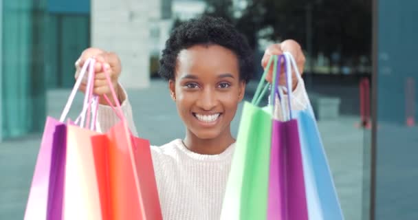 Närbild porträtt afrikansk amerikansk kvinna konsument shoppare köpare shopaholic står poserar framför kameran visar ljusa färgade påsar med shopping gåvor nya kläder glädje rabatter, försäljning koncept — Stockvideo