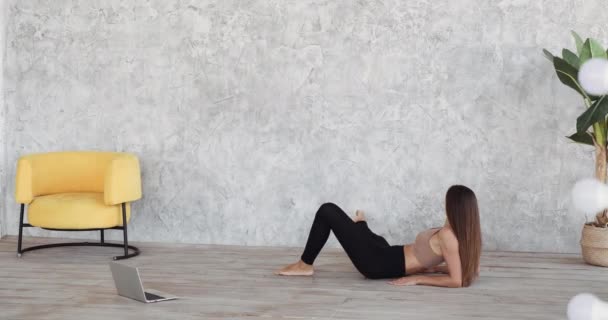 Actief gemotiveerd vrouw meisje in sportkleding ligt op de vloer kijkt naar laptop scherm herhaalt bewegingen achter online trainer heft haar benen omhoog doen abdominale oefeningen en stretching, home workout concept — Stockvideo