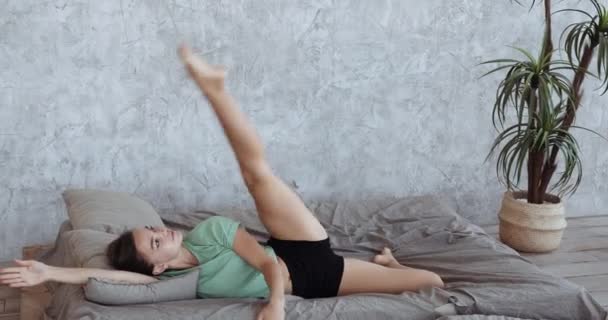 Schöne schlanke aktive Frau Mädchen in Heimkleidung Pyjama liegt in weichen bequemen Bett auf ihrer Seite hebt senkt Bein Übungen in der Früh immer bereit für den Beginn des Tages, gesunder Lebensstil — Stockvideo